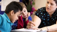 A teacher discusses writing feedback with two students.