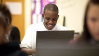 A high school student smiles confidently as he uses his computer.