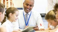 A teacher works with students seated around a table.