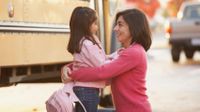 A photo of a parent and child in front of a school bus.