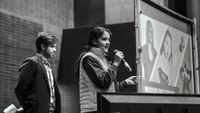 Teenage female student stands at a microphone speaking to a crowd.