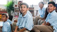 Seated on the floor, elementary school children in school uniforms look all in the same direction.