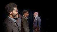 A side profile of a black educator smiling. The background is out of focus, showing three other black educators standing.