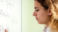 Close up of girl at white board doing a math problem