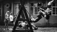 Four students are swinging on a swing set, and another student is standing by one of them.
