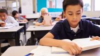 Children in a classroom read texts in books and tablet computers.