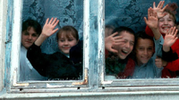 A photo of a group of elementary students looking out a window, waving and smiling.