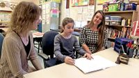 Student sharing her work with a teacher and a parent