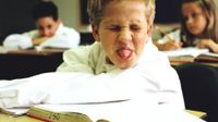 Boy sitting in class, eyes closed, nose wrinkled, sticking his tongue out
