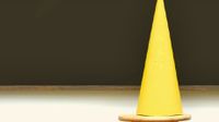 Yellow dunce cap sitting on a stool in front of a blackboard