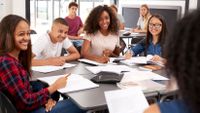 A group of smiling students have a discussion in class.