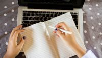A woman writes in a notebook instead of using her laptop.