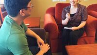 A man and woman are sitting across from each other in armchairs, smiling.