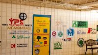 An outdoor covered hallway with 25+ logos painted on the wall and door