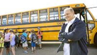 A bus driver greets students outside the bus.