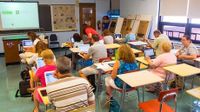 Adults in a classroom sitting at individuals desks with laptops