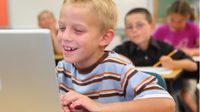 Boy at his desk laughing at something on his laptop