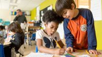 A six-year-old boy and girl sit together working on a writing assignment.