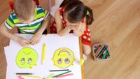 Two small children place facial expression stickers on drawings of a happy face and sad face.