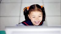 Young girl laughing in front of computer monitor