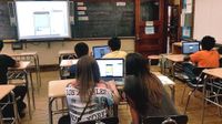 Students in class working in pairs on laptops looking at a projection on screen