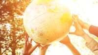 Many hands lifting up a large beach ball that looks like a globe