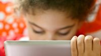 A laptop screen in the foreground with a blurred student behind the screen.