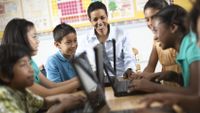 A teacher and her students discuss the work on their laptops.