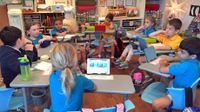 Group of eight elementary school children sitting in circle at desks, some with tablets