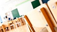 Wide shot of a tidy, well-lit classroom with lots of open space with focus on the back of a chair
