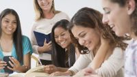 A group of high school girls have fun looking in a dictionary.
