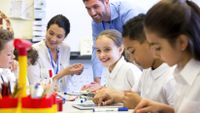 A coach looks on as a teacher works with students.