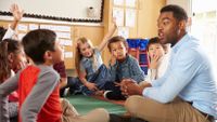 A teacher and his young students sit on the rug in a circle.