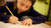 A photo of an elementary-school girl writing in her notebook with a pencil.