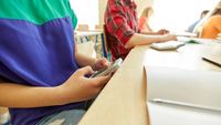 Close-up photo of a student seen only from collarbone to hip, concealing a smartphone in class