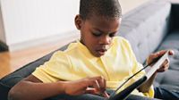 Boy sitting at end of a couch working on a tablet