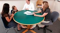 Young boy sitting between and woman and man at a round table with a teacher sitting across from them holding papers