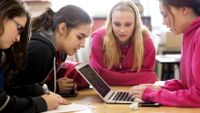 Four girls look at a laptop together in class.