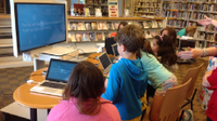 Photo of a group of students sitting around a computer lab table in the school library.