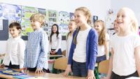A group of young students get up from their desks to move around.