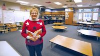 Teacher standing in empty classroom holding a book.