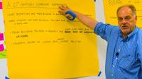 Man pointing to 21st Century Learning Experience notes on big yellow easel paper taped onto a whiteboard
