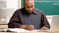 A teacher marks student writing at his desk.