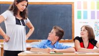 An angry-looking teacher stands with her hands on her hips beside two students.