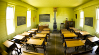 A fisheye photo of a classroom with wooden desks and a wood-burning stove.