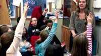 Mathis in active dialogue with students sitting in circle on the floor with hands raised