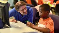 Mitch Resnick and a young boy talk while sitting at a computer.