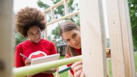 Two young women work on a building under construction.