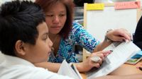 Teacher helping a boy read pointing to words in a book