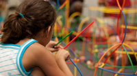 A photo of an elementary-school girl creating a model with colorful sticks.